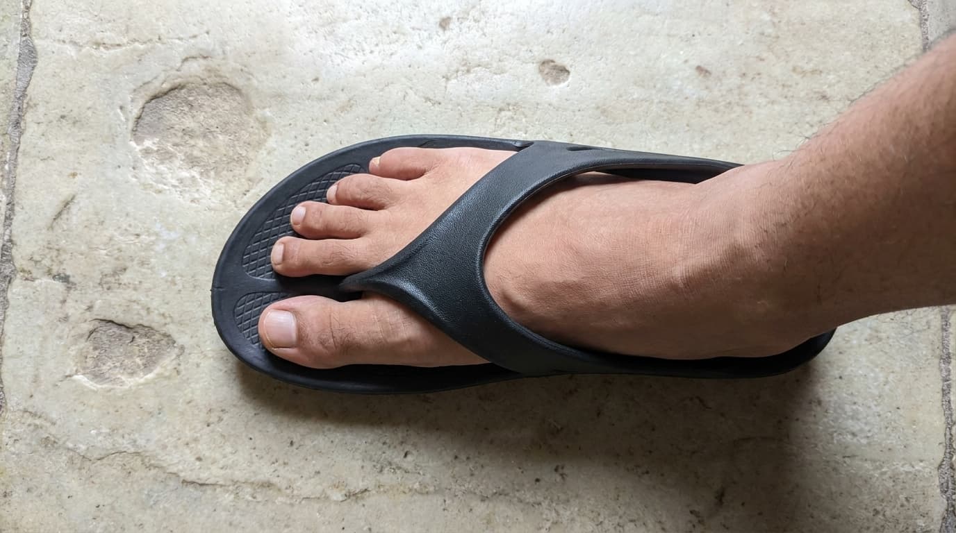 Seen from above, a broad foot in a black Fanture flip flop with room either side on the footbed