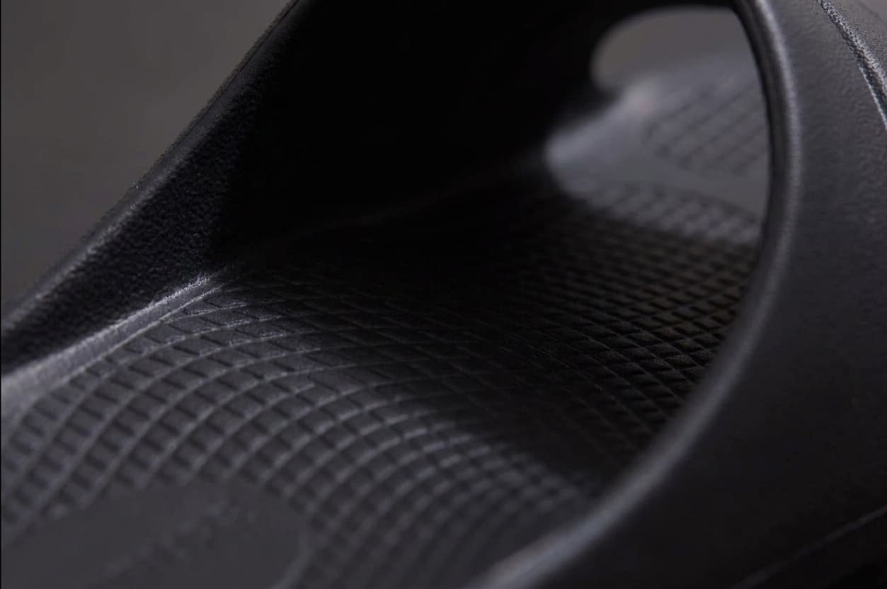 A close-up of the footbed of a black Fanture slide in raking light, showing the diamond texture and the contour rising toward the arch