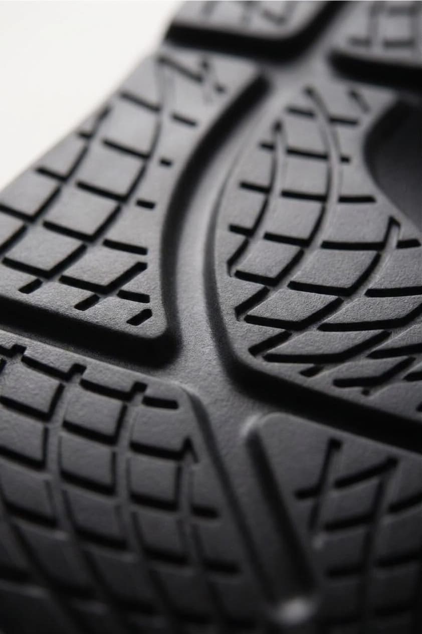 A close-up of the outsole tread of a black Fanture recovery shoe in raking light, the channels cut through the tread