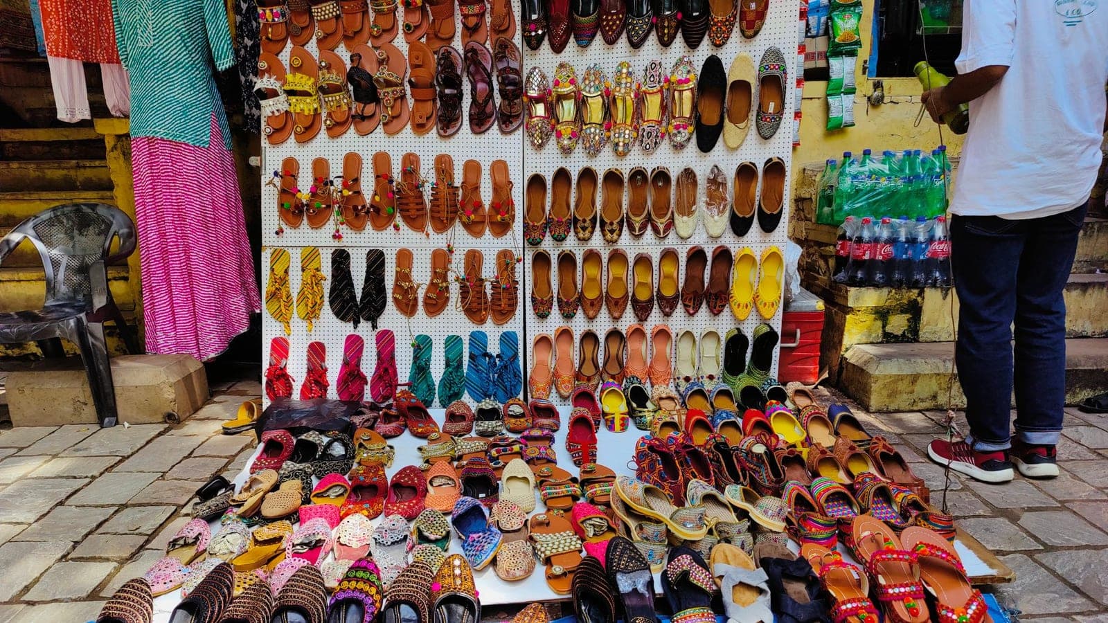 Rows of brightly coloured handmade sandals and juttis laid out side by side on a street footwear stall in Jaipur