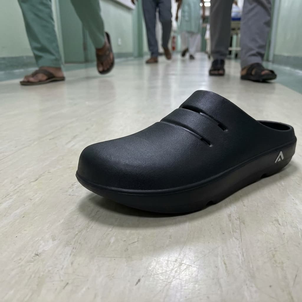 A close view of a black Fanture clog on a pale vinyl floor, the closed toe box, the holes through the upper and the thick one-piece foam sole