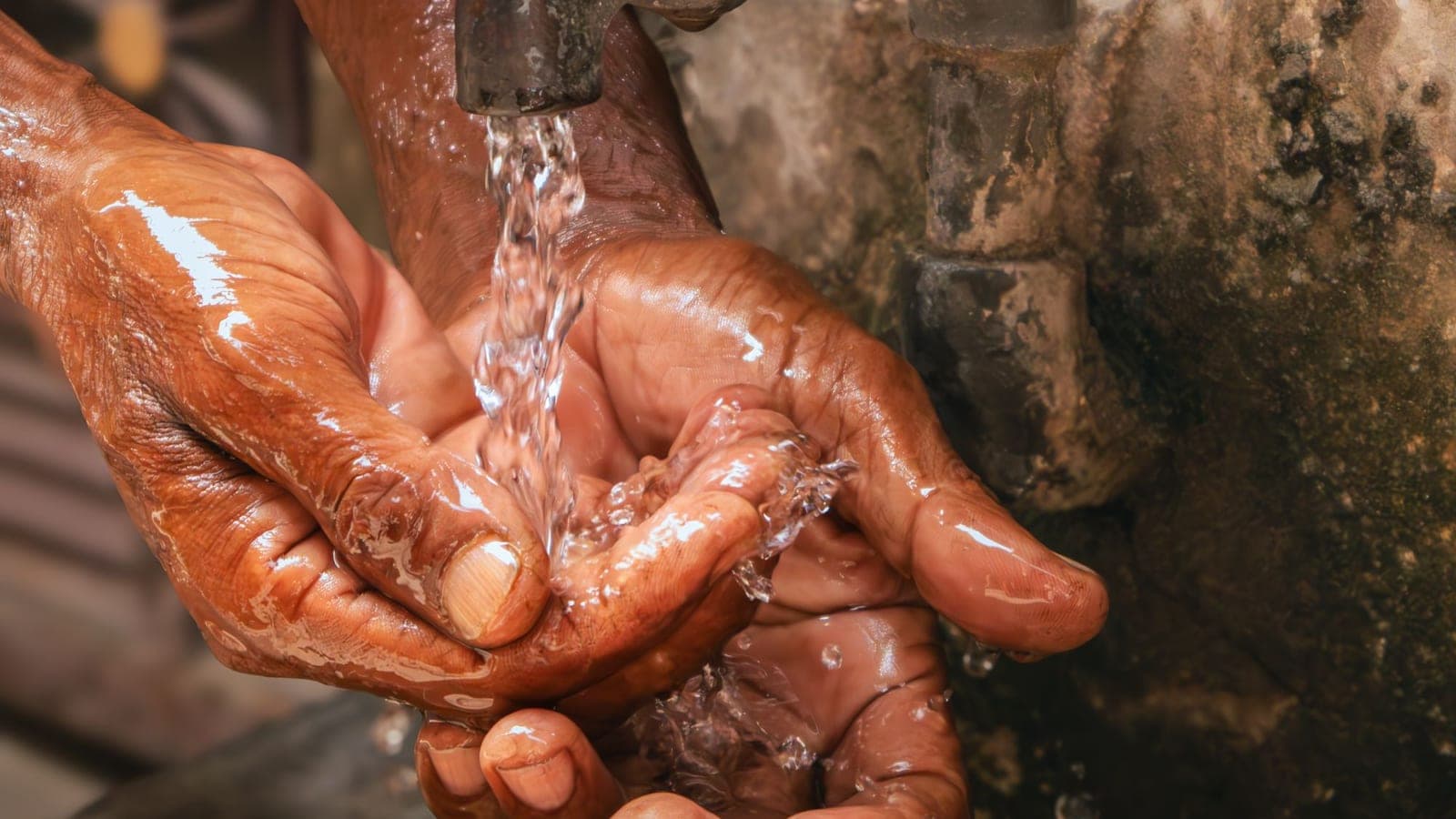 Hands held under running water at an outdoor tap, bright daylight catching the splash